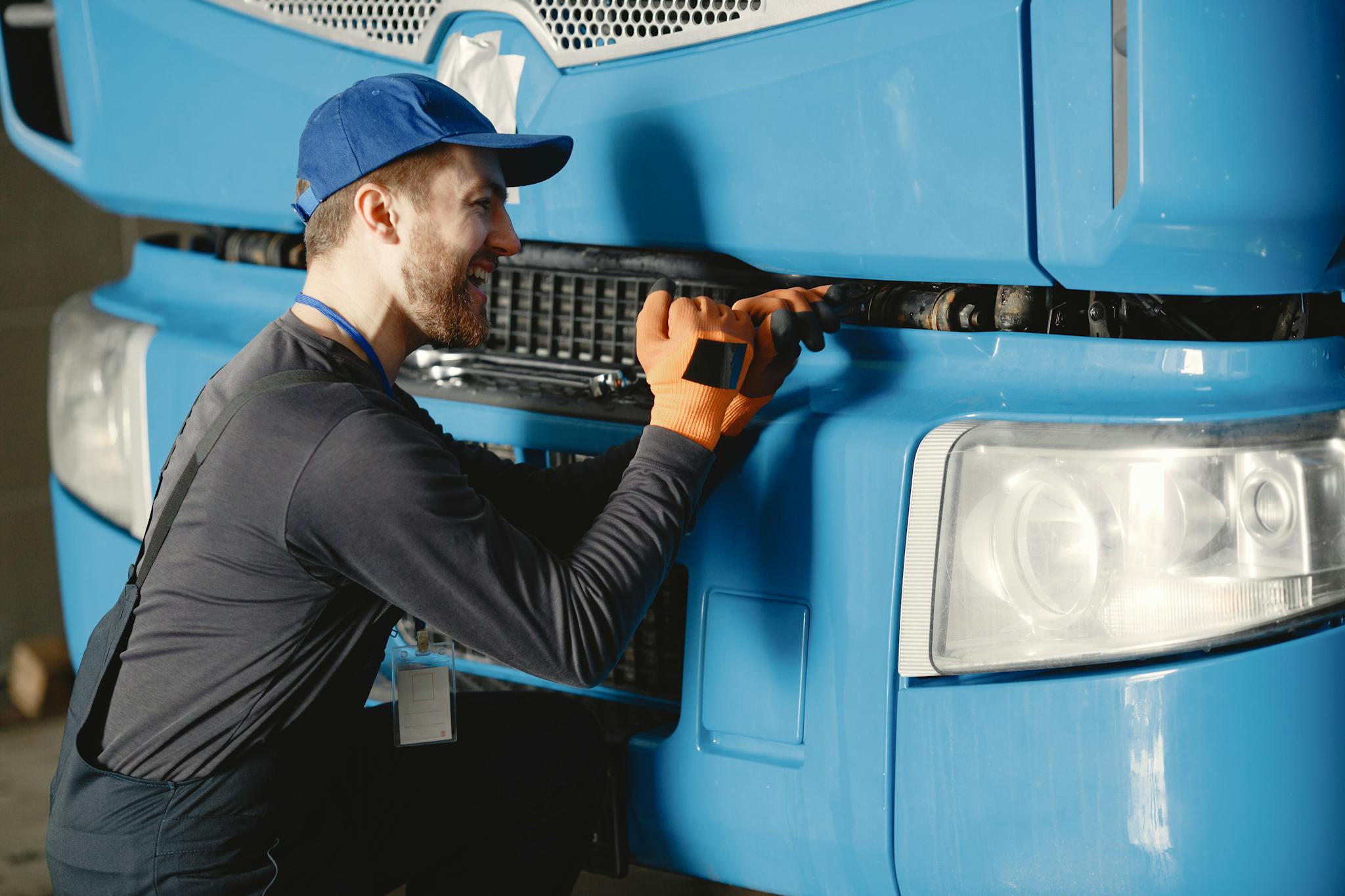 Smiling mechanic in uniform performing maintenance on a blue truck.